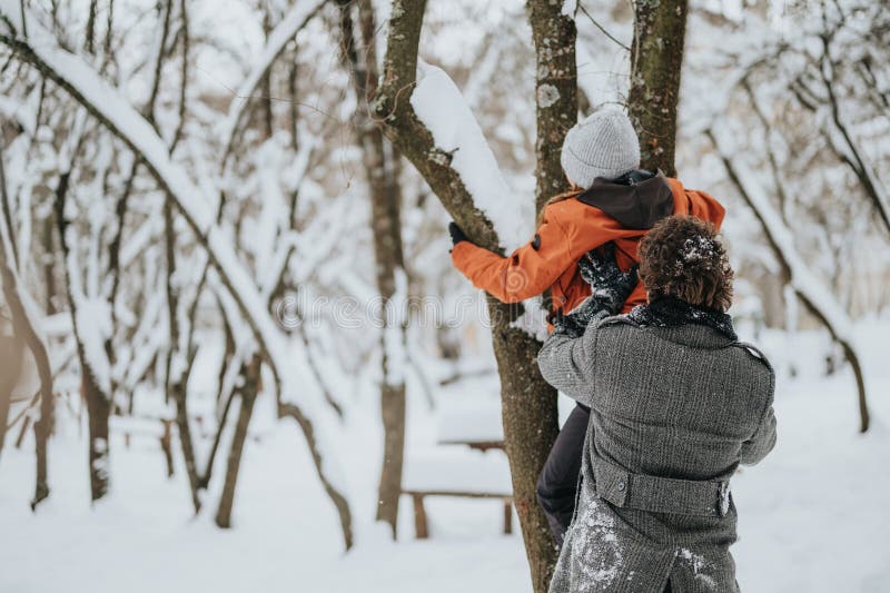 Due persone che godevano di un lugubre inverno in una foresta innevata. Una persona aiuta un altro a arrampicarsi su un albero in mezzo a un paesaggio boschivo sereno coperto di neve. Il momento trasmette gioia e unità di cure durante un freddo inverno trascorso all'aperto.