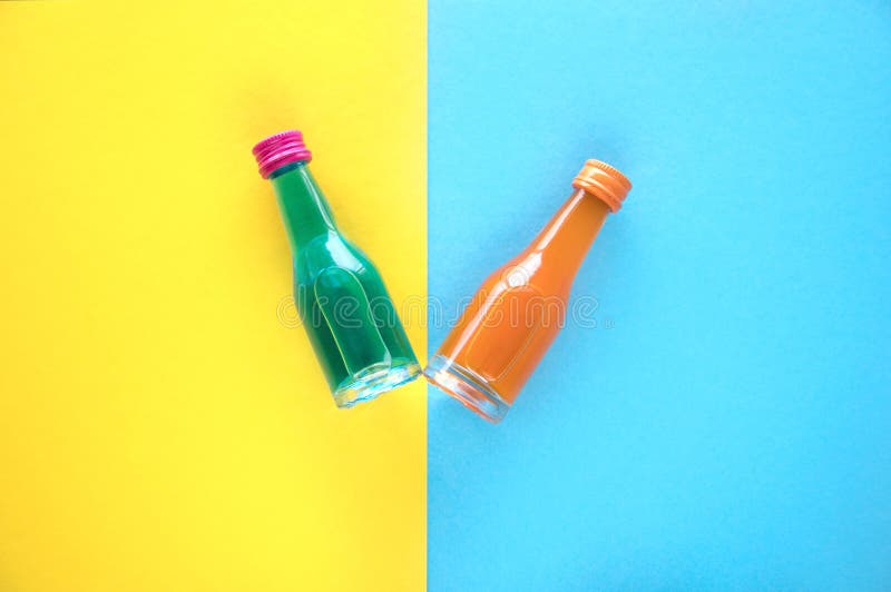 Due piccole bottiglie di vetro con un cocktail blu ed arancio su un fondo blu e giallo Due di piccole bottiglie colorate multi co immagini stock Due piccole bottiglie di vetro con un cocktail blu ed arancio su un fondo blu e giallo Due di piccole bottiglie colorate multi co immagini stock