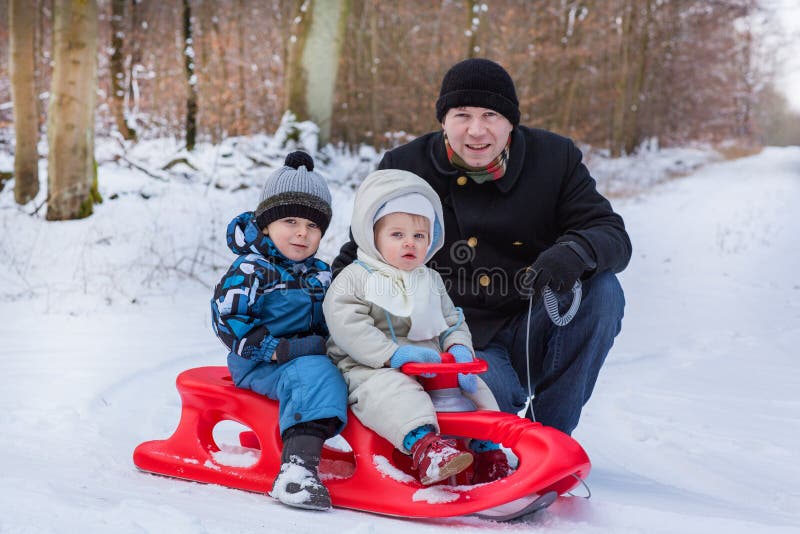 Due piccoli fratelli germani ed il loro padre divertendosi sulla slitta immagini stock Due piccoli fratelli germani ed il loro padre divertendosi sulla slitta immagini stock