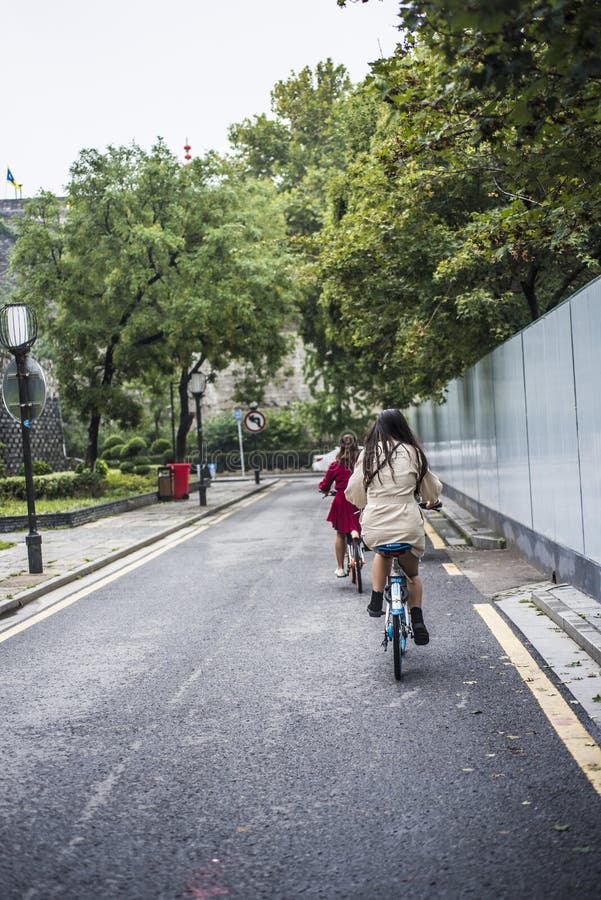 Due ragazze che guidano le biciclette senza fretta lungo il muro di cinta antico fotografie stock libere da diritti Due ragazze che guidano le biciclette senza fretta lungo il muro di cinta antico fotografie stock libere da diritti