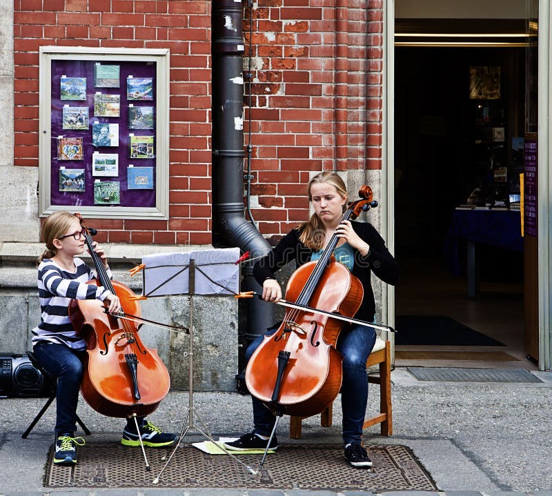 Due ragazze dell'adolescente eseguono la musica classica con i violoncelli a Monaco di Baviera. Monaco di Baviera, Germania - la musica della via, due ragazze della scuola di musica gioca il violoncello sulla via del centro di Monaco di Baviera