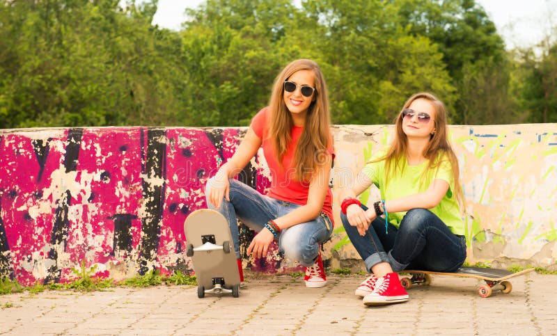 Due ragazze teenager divertendosi insieme al bordo del pattino Outd fotografia stock libera da diritti Due ragazze teenager divertendosi insieme al bordo del pattino Outd fotografia stock libera da diritti