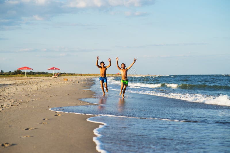 Due ragazzi felici che corrono sul mare tirano all'estate con l'AR alzata fotografie stock Due ragazzi felici che corrono sul mare tirano all'estate con l'AR alzata fotografie stock
