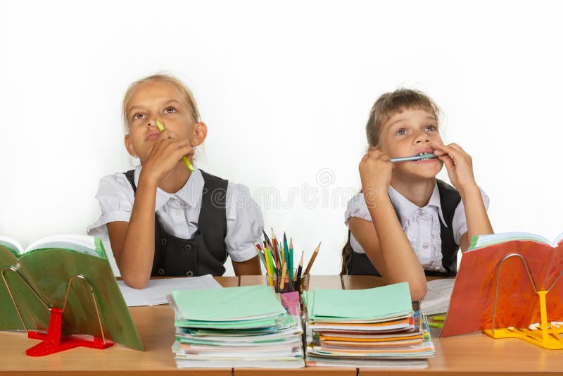 Due scolare pensively e divertenti si siedono alla tavola e cercano fotografia stock libera da diritti Due scolare pensively e divertenti si siedono alla tavola e cercano fotografia stock libera da diritti