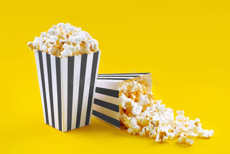Due secchi di cartone a strisce bianche e nero con popcorn di formaggio saporito isolati su fondo giallo immagini stock libere da diritti