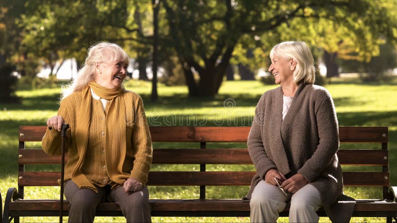 Due signore anziane che ridono e che parlano, sedentesi sul banco in parco, vecchi amici immagini stock libere da diritti Due signore anziane che ridono e che parlano, sedentesi sul banco in parco, vecchi amici immagini stock libere da diritti