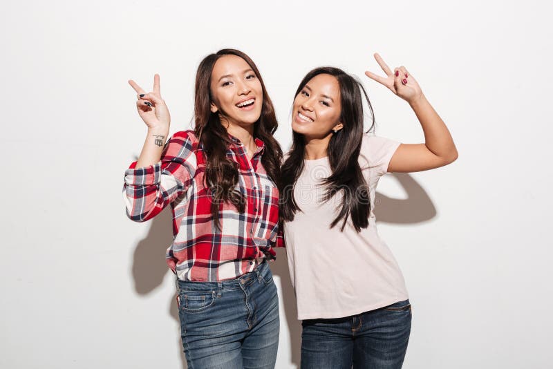 Image of two asian pretty cheerful ladies sisters hugging with each other. Looking camera showing peace gesture. Image of two asian pretty cheerful ladies sisters hugging with each other. Looking camera showing peace gesture.