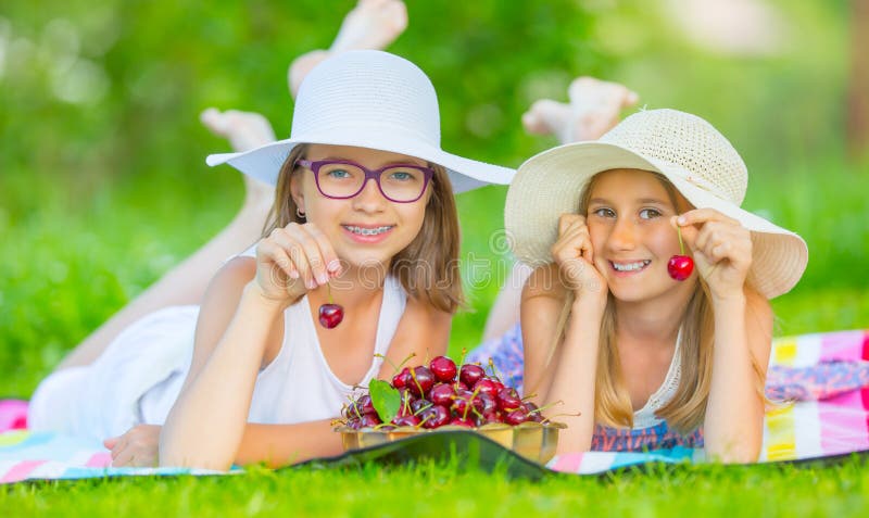 Due sorelle o amici svegli in un giardino di picnic si trovano su una piattaforma e mangiano le ciliege di recente selezionate fotografia stock Due sorelle o amici svegli in un giardino di picnic si trovano su una piattaforma e mangiano le ciliege di recente selezionate fotografia stock