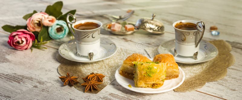Two cups of Turkish coffee and glasses of water and a plate with baklava lukum in lukumluk decorative flowers and badyan on a sunny day on a wooden table vintage toned picture close-up shallow depth of field. Two cups of Turkish coffee and glasses of water and a plate with baklava lukum in lukumluk decorative flowers and badyan on a sunny day on a wooden table vintage toned picture close-up shallow depth of field