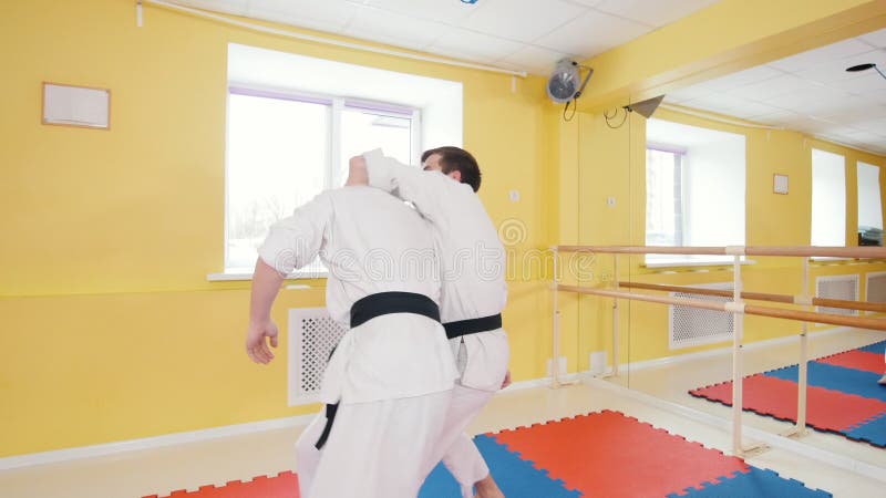 Due uomini atletici che preparano le loro abilità di aikidi nello studio Schiva il colpo ed il lancio dell'oppositore sul pavimen