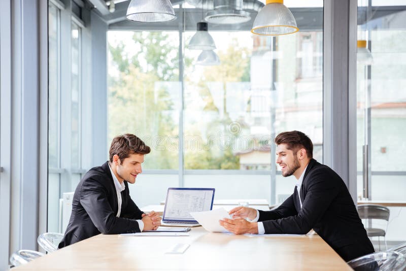 Due uomini d'affari felici che lavorano insieme facendo uso del computer portatile sulla riunione d'affari immagini stock libere da diritti Due uomini d'affari felici che lavorano insieme facendo uso del computer portatile sulla riunione d'affari immagini stock libere da diritti