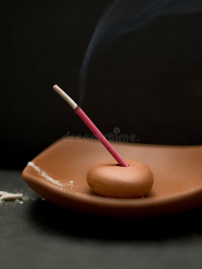 Red scented incense stick burning in holder with smoke with a black background. Red scented incense stick burning in holder with smoke with a black background.