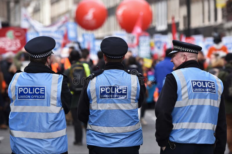 London, UK - March 4, 2017. Police look-on as protesters march during a demonstration in support of the NHS. Thousands marched against NHS spending cuts, hospital closures and privatisation. London, UK - March 4, 2017. Police look-on as protesters march during a demonstration in support of the NHS. Thousands marched against NHS spending cuts, hospital closures and privatisation.