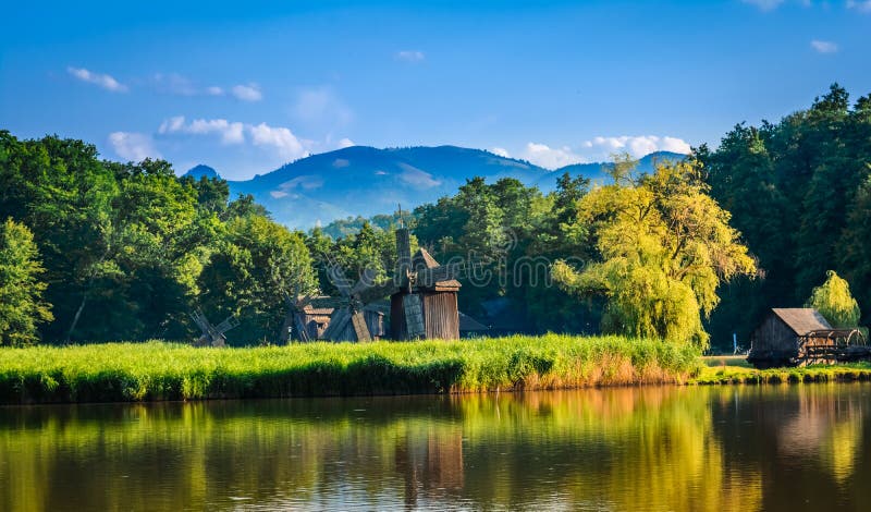 Dumbrava, Sibiu, Romania: Landscape of a lake with windmill in the golden light before sunset. Dumbrava, Sibiu, Romania: Landscape of a lake with windmill in the golden light before sunset.