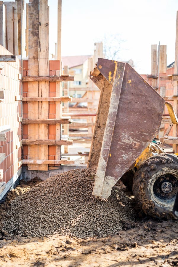 Dumper truck unloading construction gravel, granite and crushed stones at building foundation