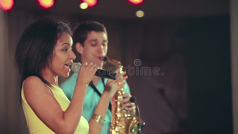 Dunkelhäutiger Sänger der schwarzen Frau und dünner Saxophonspieler, die am Stadium durchführt