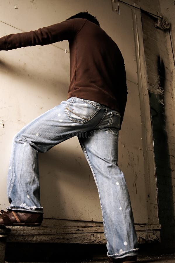 Thin male in distressed jeans posed near a dirty white door, he's wearing a brown fashionable shirt. Thin male in distressed jeans posed near a dirty white door, he's wearing a brown fashionable shirt