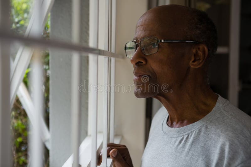 Durchdachte tragende Brillen des älteren Mannes beim durch Fenster heraus schauen lizenzfreies stockbild Durchdachte tragende Brillen des älteren Mannes beim durch Fenster heraus schauen lizenzfreies stockbild