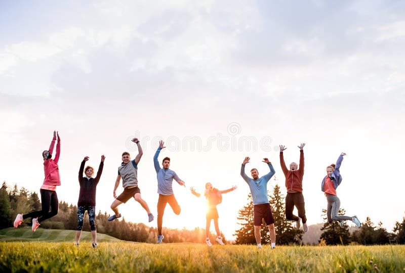 Duża grupa sprawnych i aktywnych ludzi skaczących po ćwiczeniach w naturze