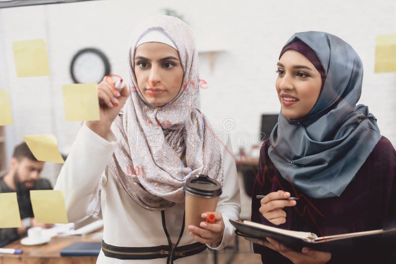 Dwa arabskiej kobiety pracuje w biurze Coworkers biorą notatki na szkło desce