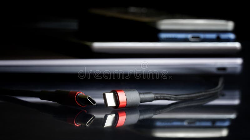 Two red and black usb type-c connectors next to many modern gadgets: laptop, tablet and smartphones. Modern way to connect, transfer data and charge gadgets. Selective focus. Macro. Two red and black usb type-c connectors next to many modern gadgets: laptop, tablet and smartphones. Modern way to connect, transfer data and charge gadgets. Selective focus. Macro