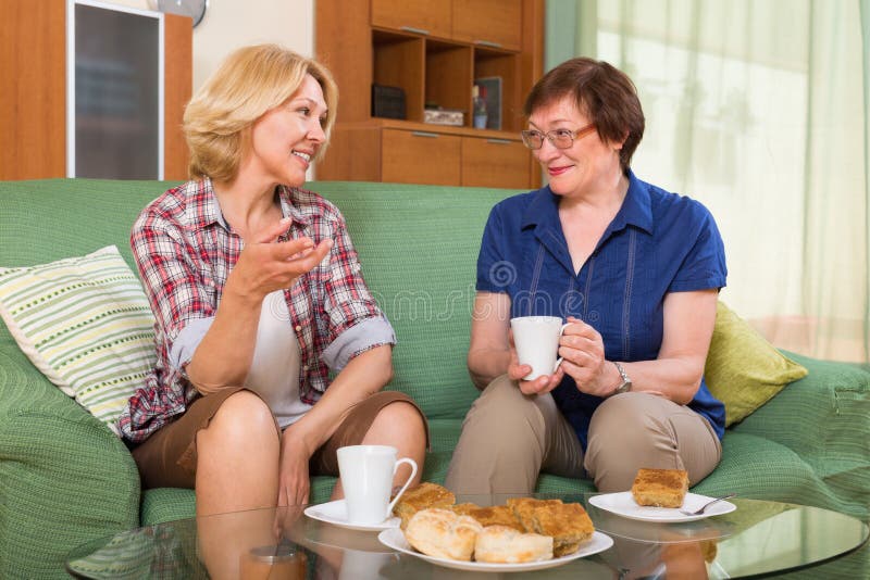 Two positive mature women friends drinking tea and gossiping at home. Two positive mature women friends drinking tea and gossiping at home