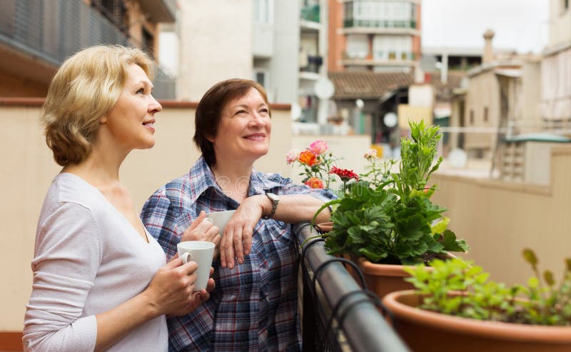 Two mature women drinking tea on balcony and smiling. Two mature women drinking tea on balcony and smiling