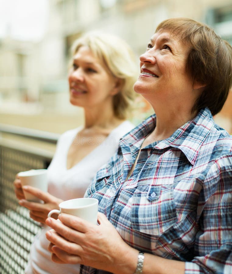 Two mature women drinking tea on terrace and smiling. Two mature women drinking tea on terrace and smiling