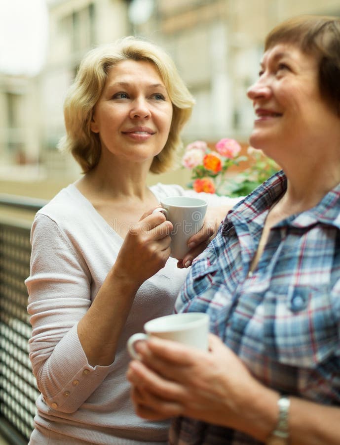 Two mature women drinking coffee on terrace and smiling. Two mature women drinking coffee on terrace and smiling