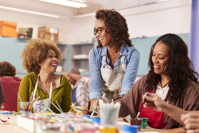 Two Mature Women Attending Art Class In Community Centre With Teacher. Two Mature Women Attending Art Class In Community Centre With Teacher