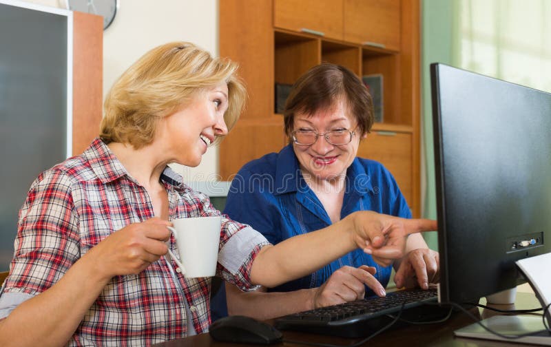 Two smiling mature women friends drinking tea and browsing web. Two smiling mature women friends drinking tea and browsing web