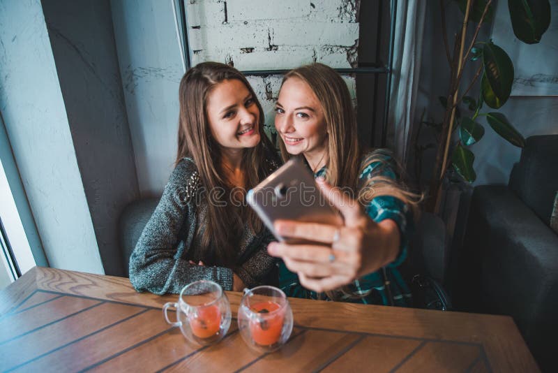 Dwa dziewczyny bierze selfie podczas gdy siedzący w kawiarni obrazy stock Dwa dziewczyny bierze selfie podczas gdy siedzący w kawiarni obrazy stock