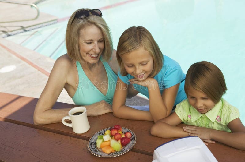 Two Girls (7-9) and Grandmother Watching portable television by swimming pool. Two Girls (7-9) and Grandmother Watching portable television by swimming pool.