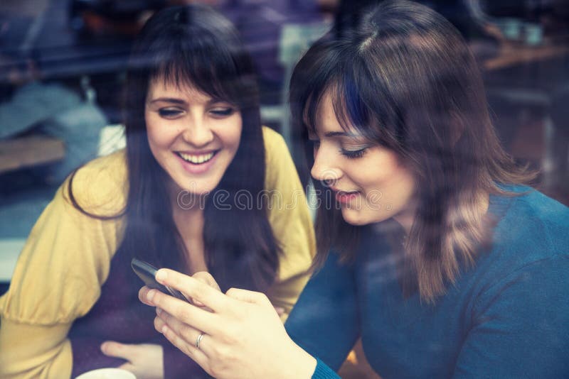 Dwa dziewczyny uśmiecha się mądrze telefon i używa w kawiarni obraz royalty free Dwa dziewczyny uśmiecha się mądrze telefon i używa w kawiarni obraz royalty free