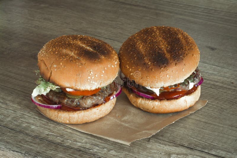 Dwa hamburgeru na sezamowych babeczkach z tłustoszowatymi wołowina pasztecikami i świeżymi sałatkowymi składnikami na zmiętym bro zdjęcia royalty free Dwa hamburgeru na sezamowych babeczkach z tłustoszowatymi wołowina pasztecikami i świeżymi sałatkowymi składnikami na zmiętym bro zdjęcia royalty free
