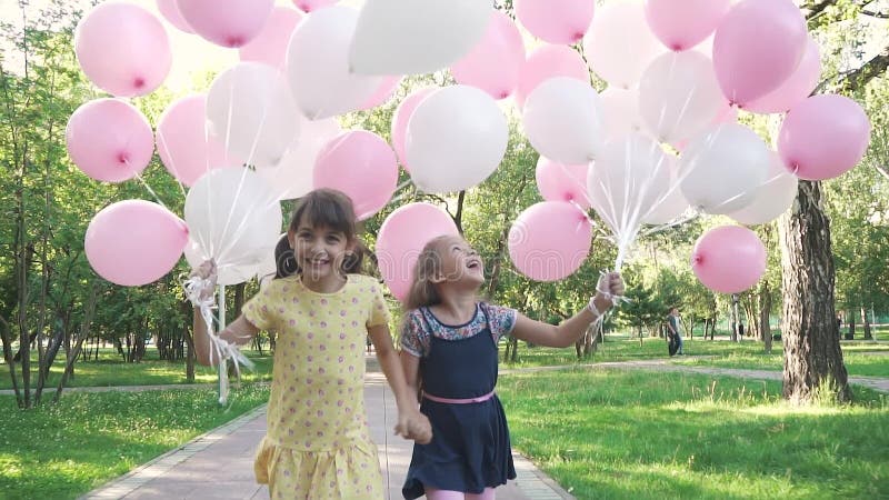 Dwa małej dziewczynki radośnie biegają przez lata parka z balonami w jego rękach małe siostry trzyma ręki i
