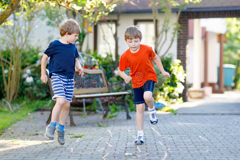 Dwa małej szkoły i preschool dzieciaków chłopiec bawić się hopscotch na boisku obrazy stock Dwa małej szkoły i preschool dzieciaków chłopiec bawić się hopscotch na boisku obrazy stock