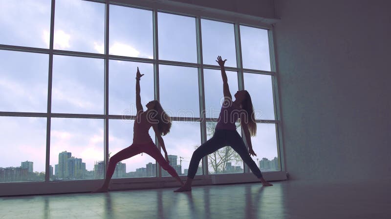 Dwa nikłej joga kobiety ćwiczy rozszerzoną trójbok pozę w studiu z naturalnym światłem