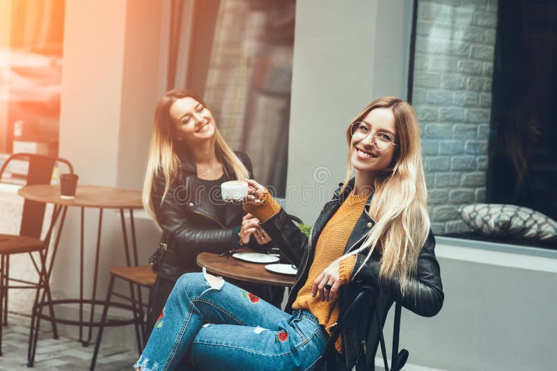 Dwa pięknej młodej kobiety opowiada kawę i pije w mod ubraniach ma odpoczynek w restauracyjny plenerowym zdjęcie royalty free