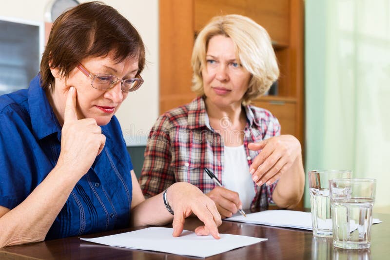 Two sad mature women looking documents at table. Two sad mature women looking documents at table