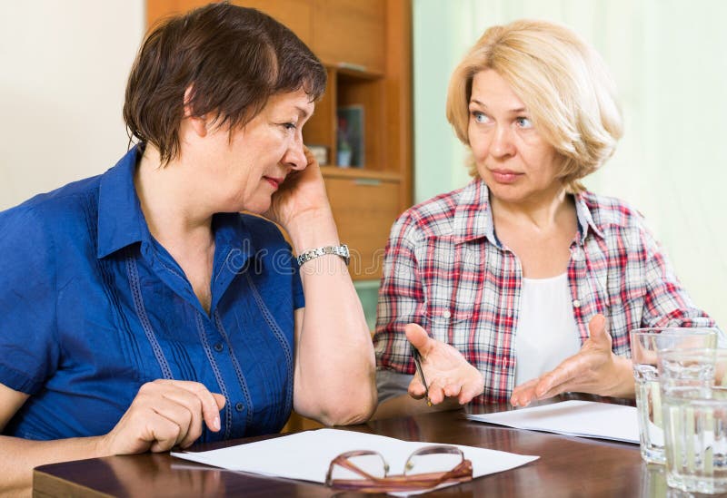 Two sad mature women with documents at table. Two sad mature women with documents at table