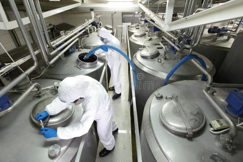 Two specialists in white protective overalls and goggles working with industrial process tanks in plant. Two specialists in white protective overalls and goggles working with industrial process tanks in plant