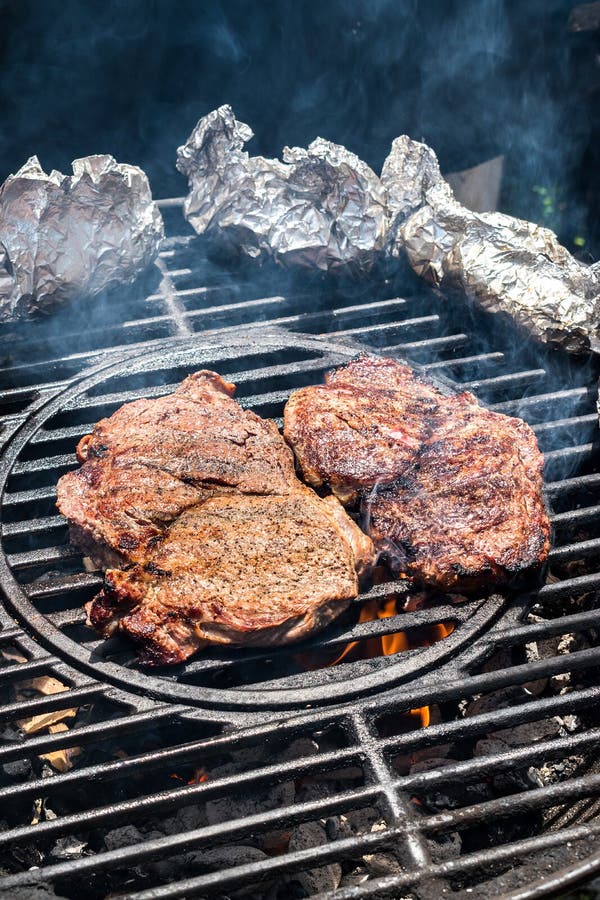 Dwa stku na round grillu z tinfoil popierają kogoś nad pożarniczym pionowo układem obraz stock Dwa stku na round grillu z tinfoil popierają kogoś nad pożarniczym pionowo układem obraz stock
