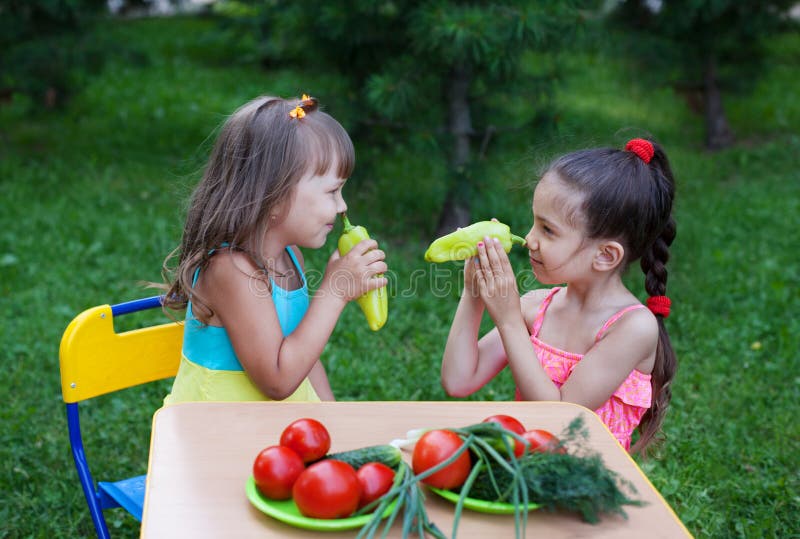 Two happy girls kids children wearing beautiful dresses holding pepper as nose and smiling. Two happy girls kids children wearing beautiful dresses holding pepper as nose and smiling