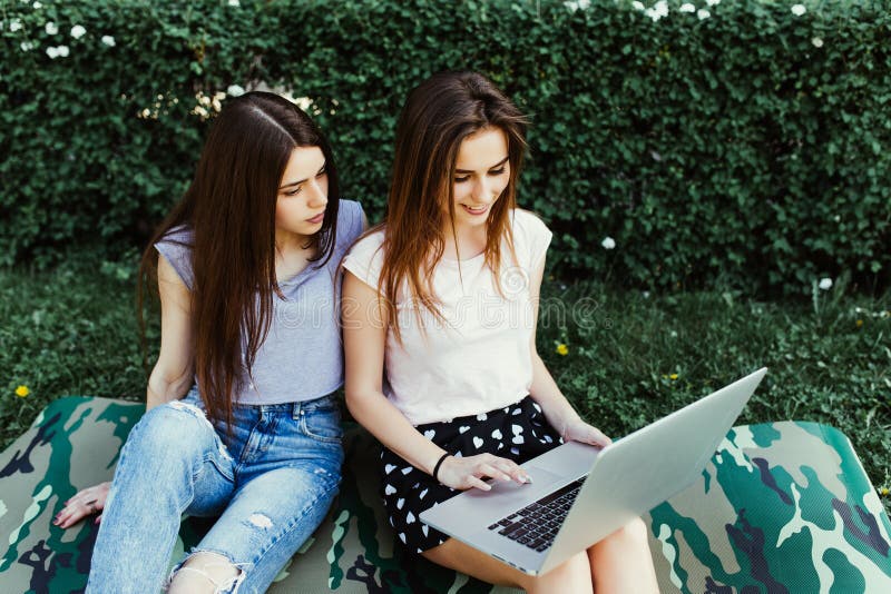 Dwa szczęśliwego przyjaciela szuka online w laptopu obsiadaniu na trawie w ulicie zdjęcie stock Dwa szczęśliwego przyjaciela szuka online w laptopu obsiadaniu na trawie w ulicie zdjęcie stock