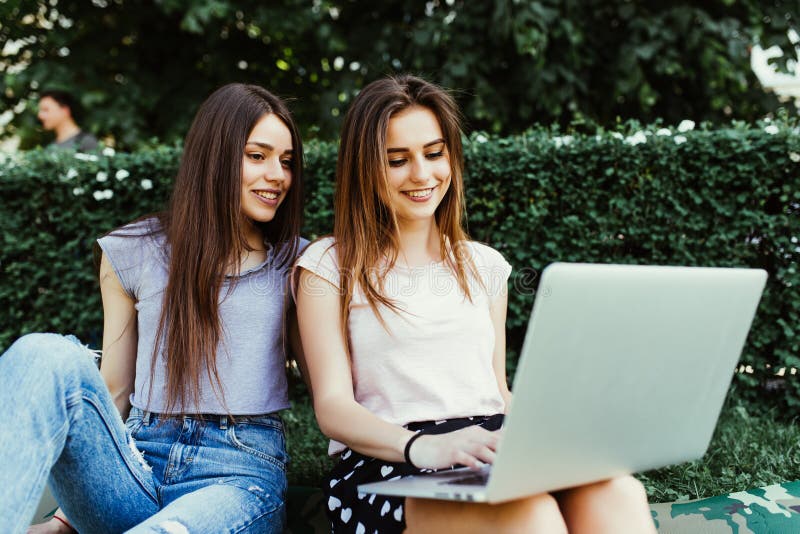 Dwa szczęśliwego przyjaciela szuka online w laptopu obsiadaniu na trawie w ulicie obraz stock Dwa szczęśliwego przyjaciela szuka online w laptopu obsiadaniu na trawie w ulicie obraz stock
