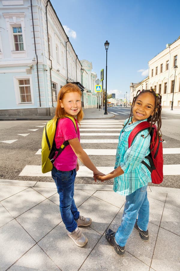 Two happy girls hold hands and stand near crossroad and smile in city during summer. Two happy girls hold hands and stand near crossroad and smile in city during summer