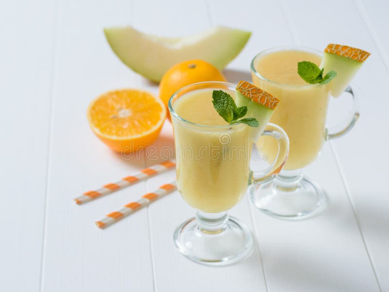 Dwa szklanego kubka z melonowym smoothie, pomarańcze i melonem na białym drewnianym stole, zdjęcie royalty free Dwa szklanego kubka z melonowym smoothie, pomarańcze i melonem na białym drewnianym stole, zdjęcie royalty free