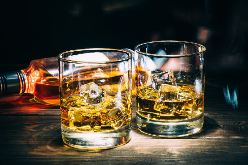 Dwa szkła scotch whisky lub koniak z kostka lodu i butelką alkoholu trunek na ciemnym drewnianym tle zdjęcia royalty free Dwa szkła scotch whisky lub koniak z kostka lodu i butelką alkoholu trunek na ciemnym drewnianym tle zdjęcia royalty free