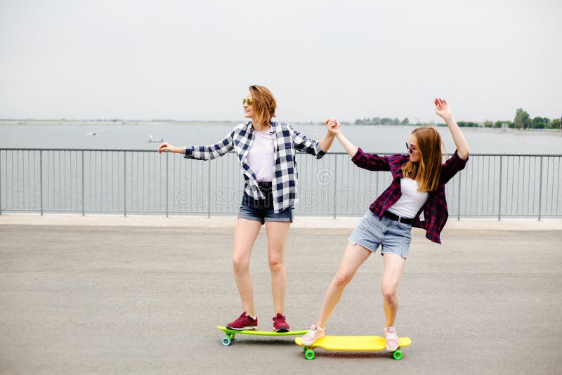 Dwa uśmiechniętego żeńskiego przyjaciela uczy się jeździeckiego longboard z pomagać each inny tła pojęcia ciemny przyjaźni pelika zdjęcie stock Dwa uśmiechniętego żeńskiego przyjaciela uczy się jeździeckiego longboard z pomagać each inny tła pojęcia ciemny przyjaźni pelika zdjęcie stock